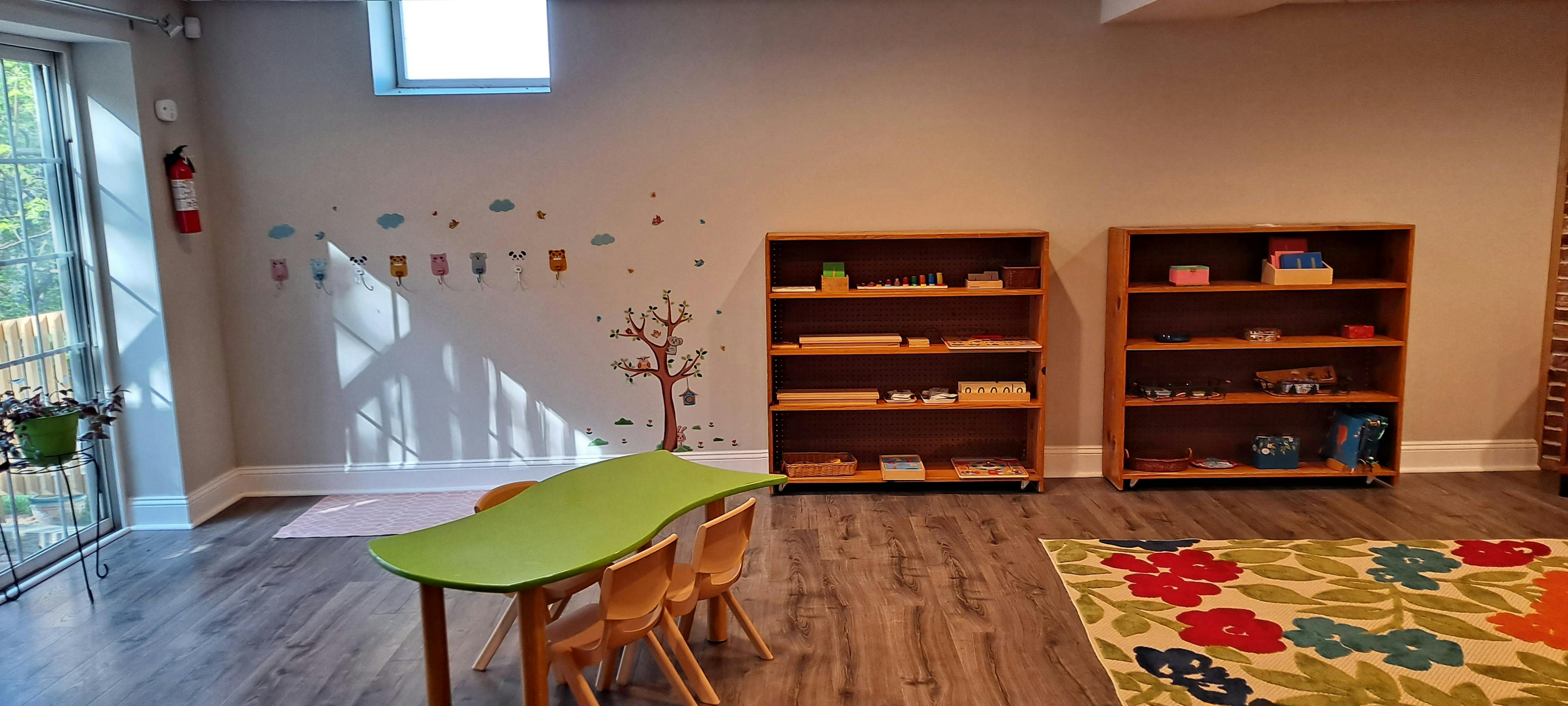 Classroom with small green table and chairs, two wooden shelves, and a colorful rug