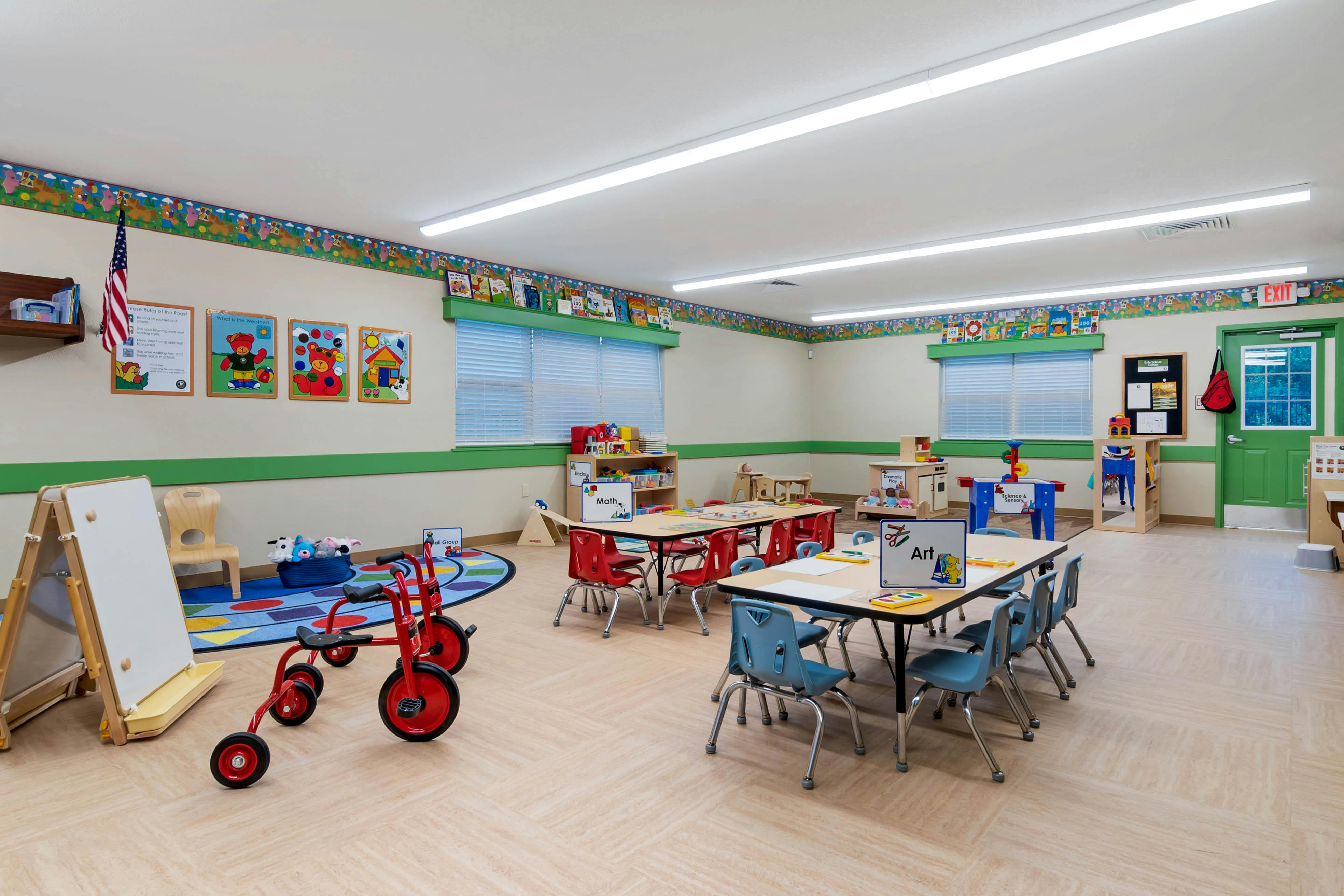 An empty early childhood classroom with small tables and chairs, toys, and learning posters