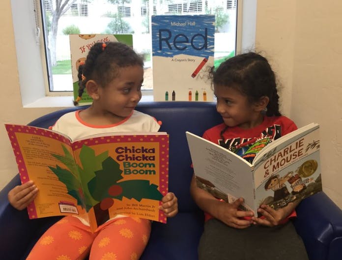 Two children sitting on a couch reading books