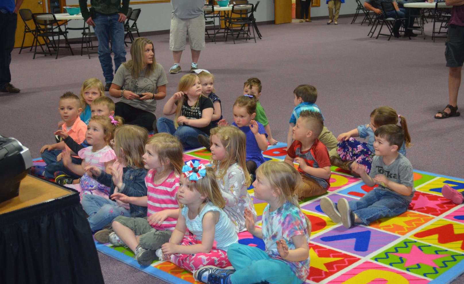 Group of children sitting on a colorful mat watching something