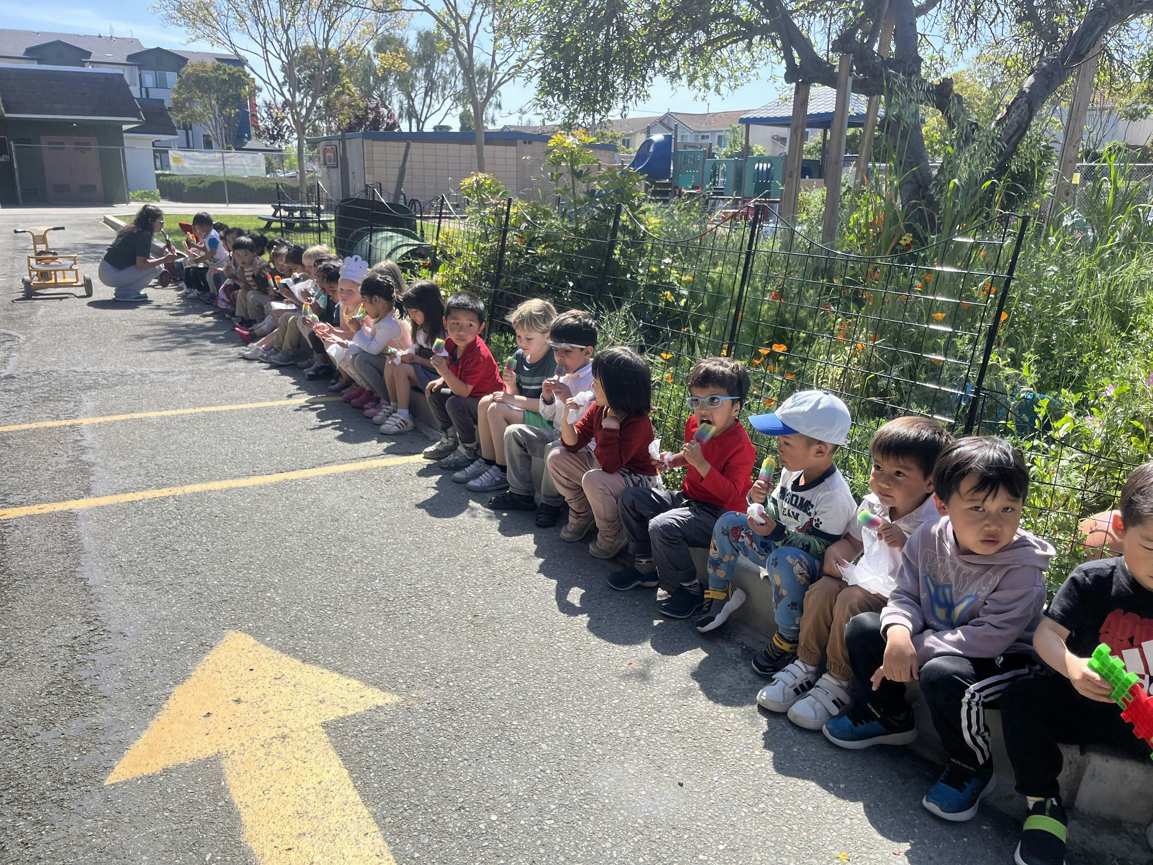 Children sitting in a line outdoors with an adult kneeling in front of them