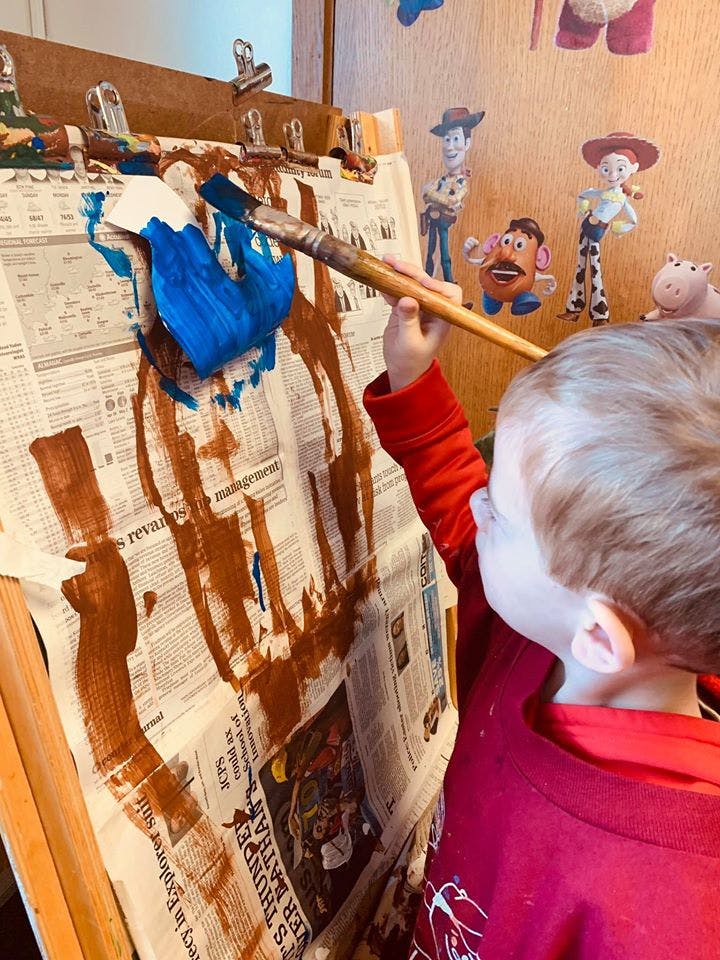 Child painting on newspaper with blue and brown paint