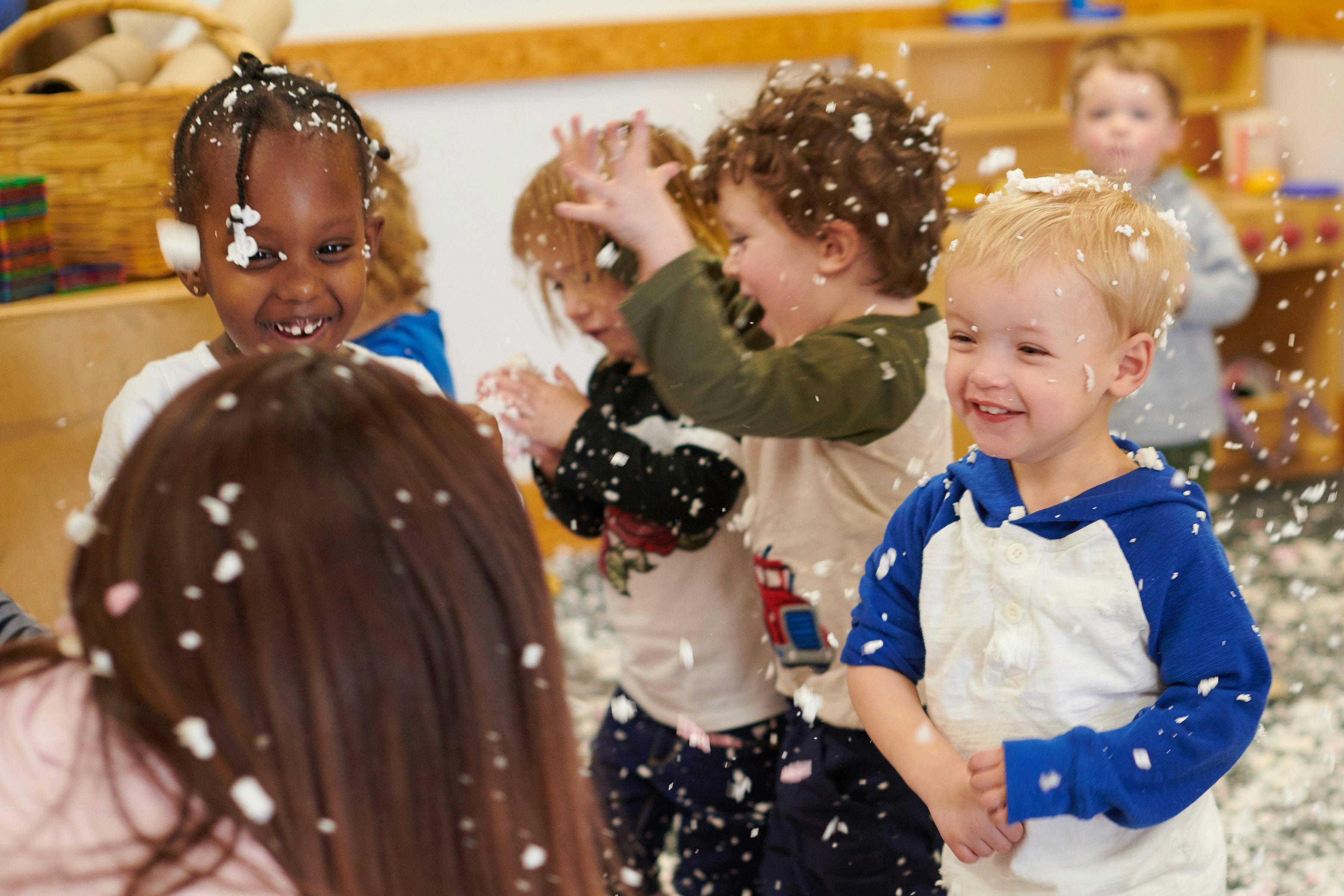 Children playing with white confetti or foam in a classroom