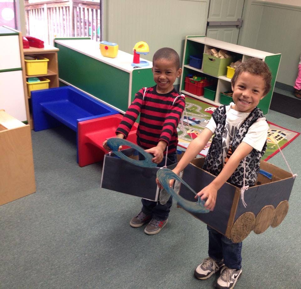 Two children playing with cardboard box cars in a classroom