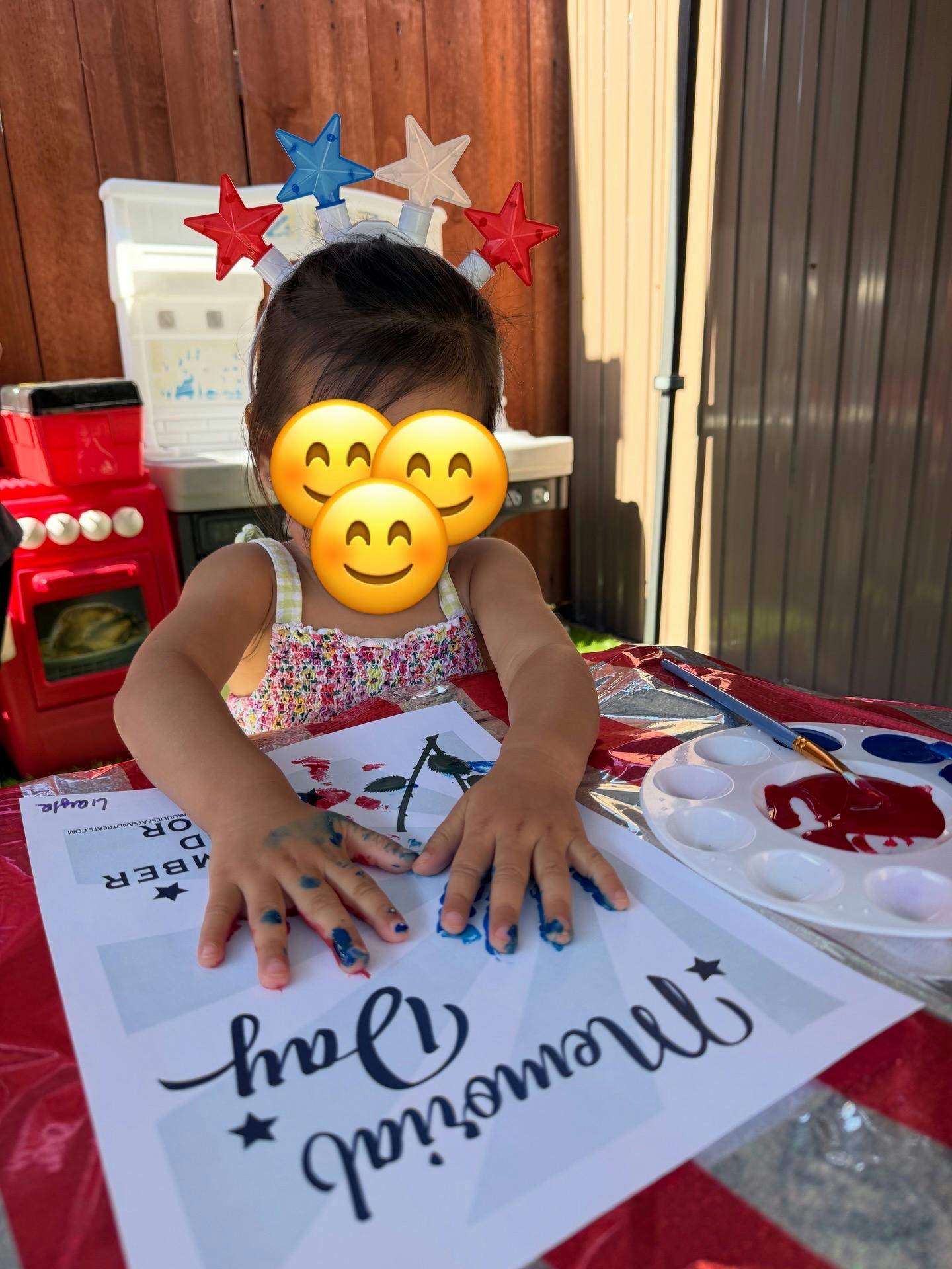 Child with star headband making a handprint painting with "Memorial Day" on paper