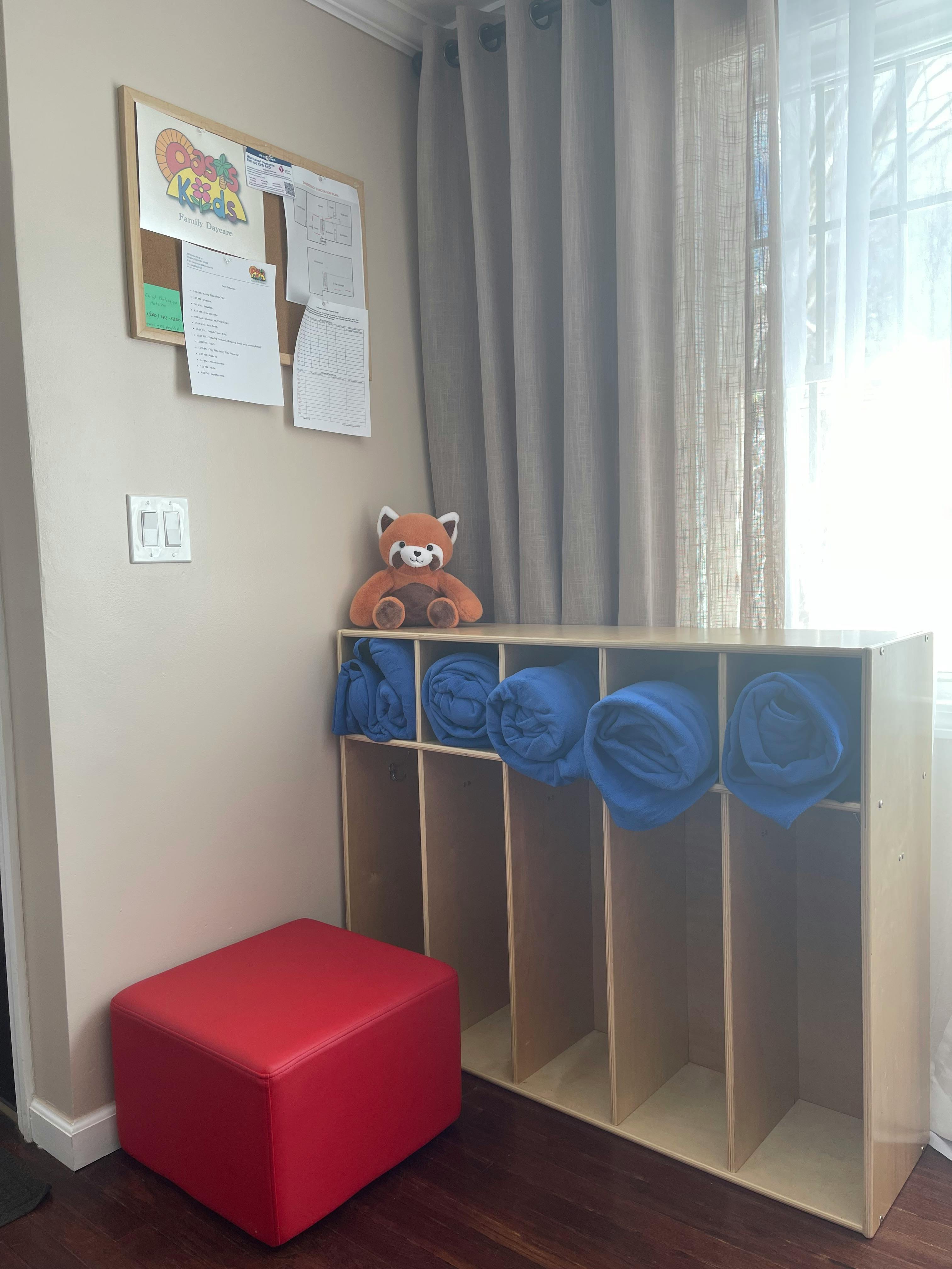 Stuffed animal on a cubby shelf with blue blankets, a red ottoman, and a bulletin board