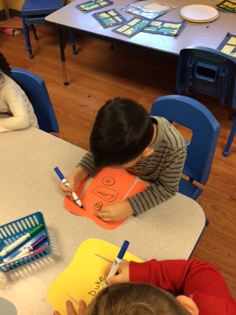 Child drawing on orange paper with a marker in a classroom
