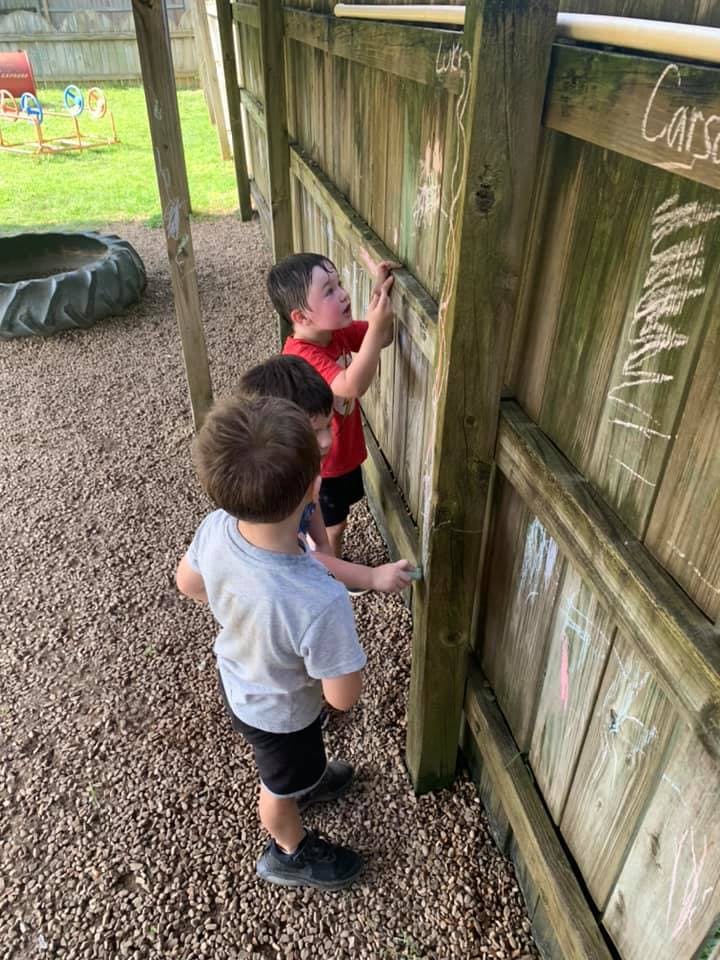 Two children drawing on a wooden fence with chalk