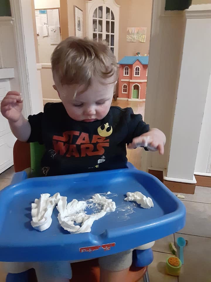 Child in a high chair playing with white food on the tray