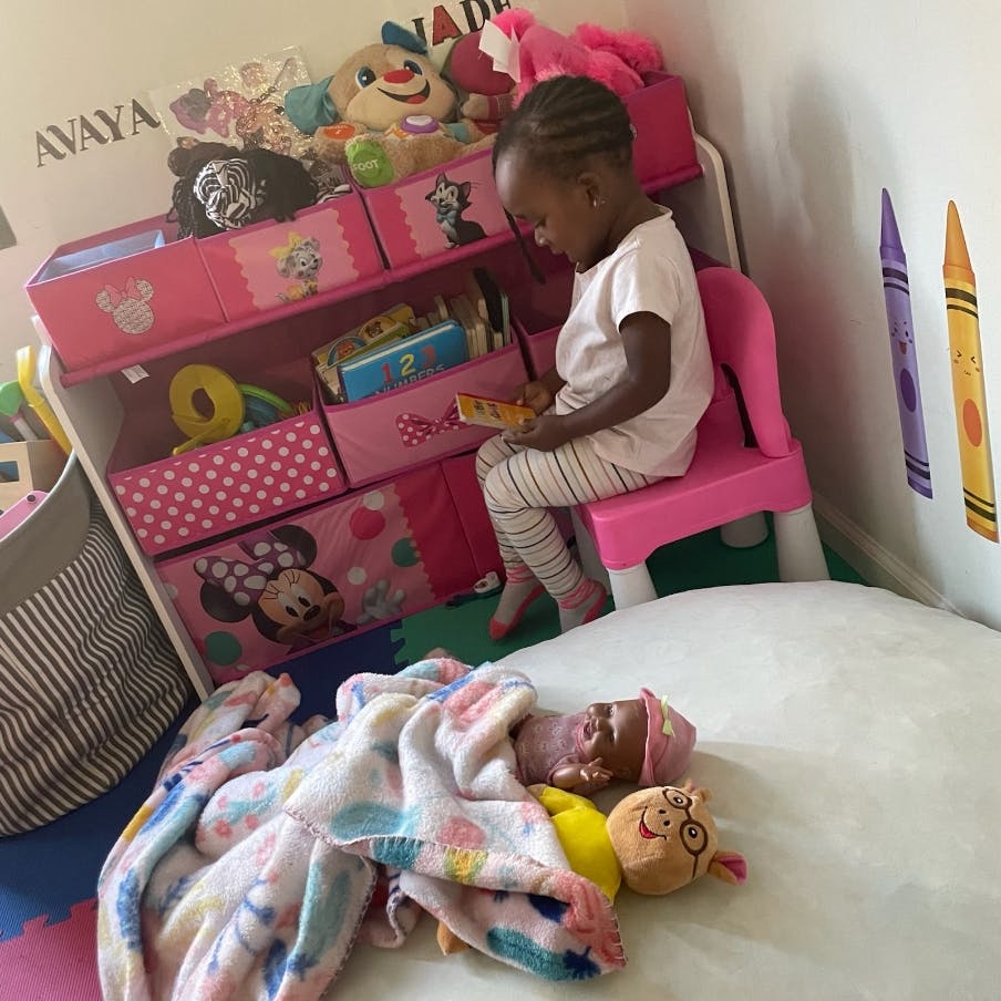 Child sitting on a pink chair reading a book next to a toy organizer