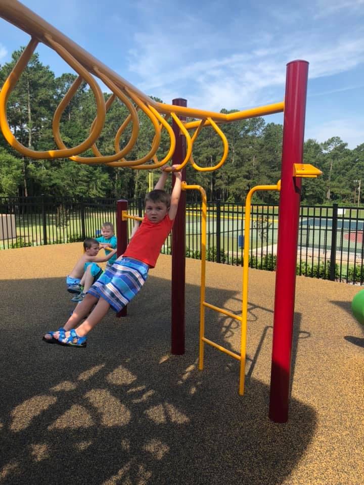 Child in red shirt swinging on monkey bars at a playground