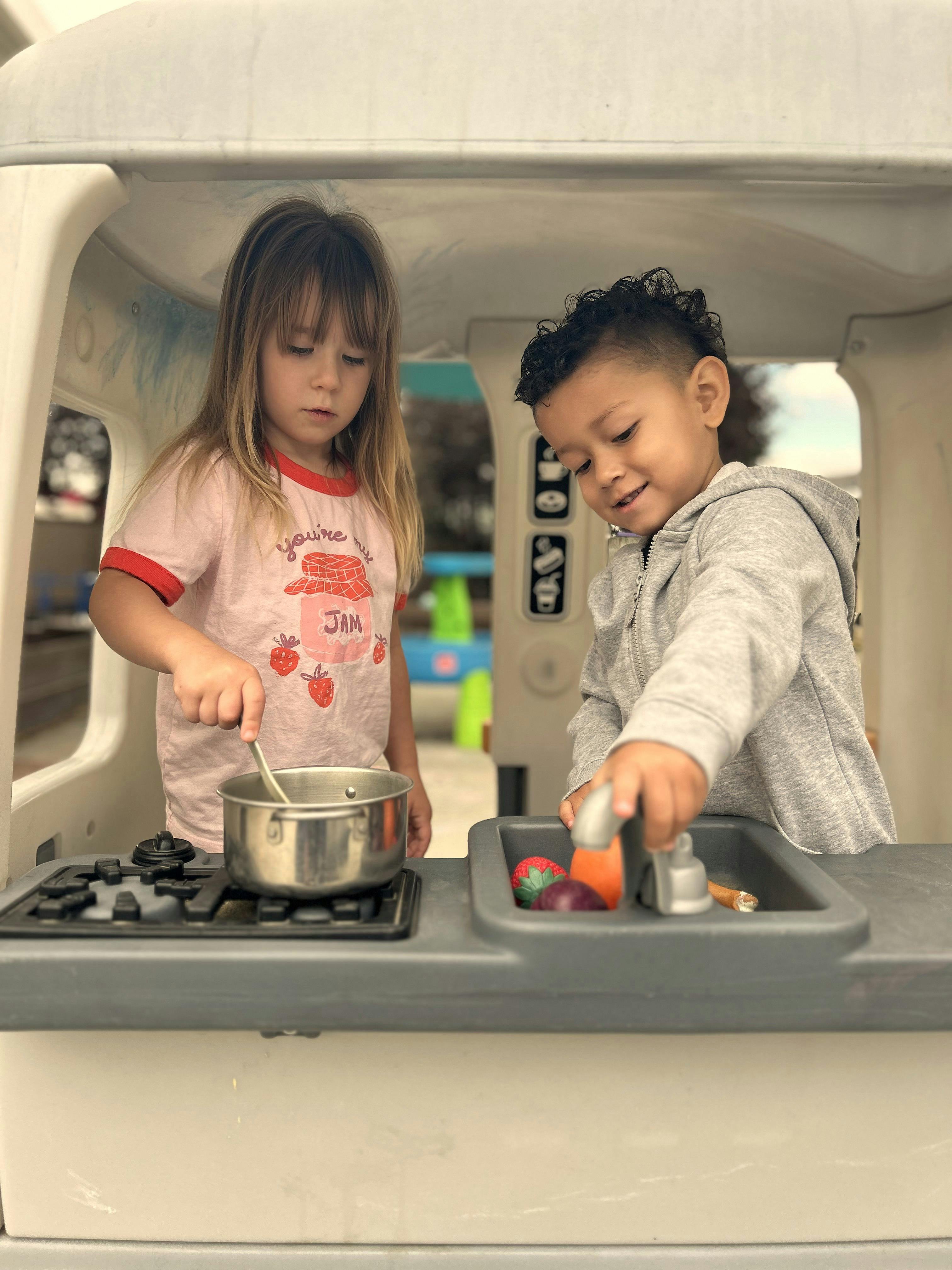 Two children playing with a toy kitchen