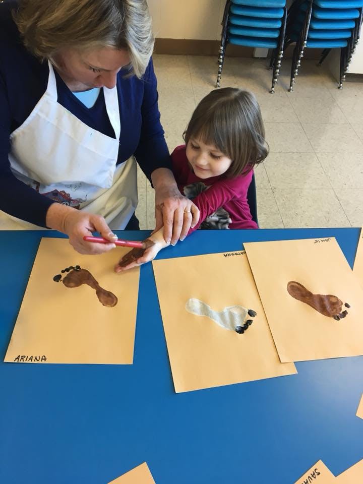 Person helping a child paint their hand over a table with footprint art