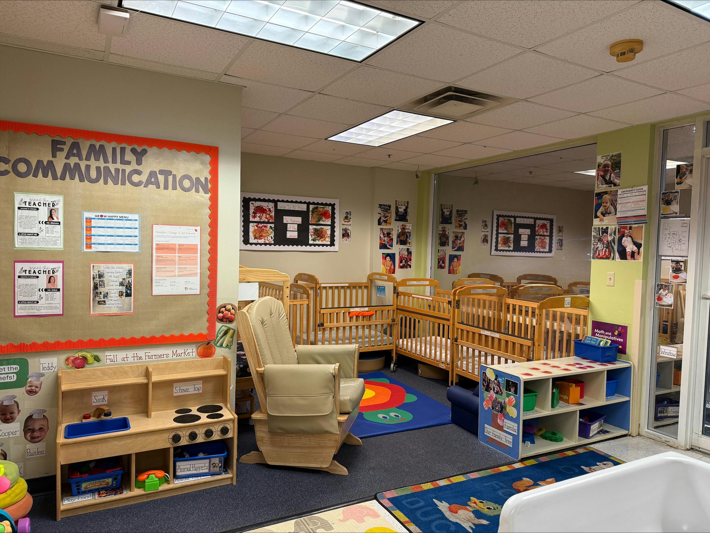 Classroom with multiple cribs, a rocking chair, a toy kitchen, and a "Family Communication" board