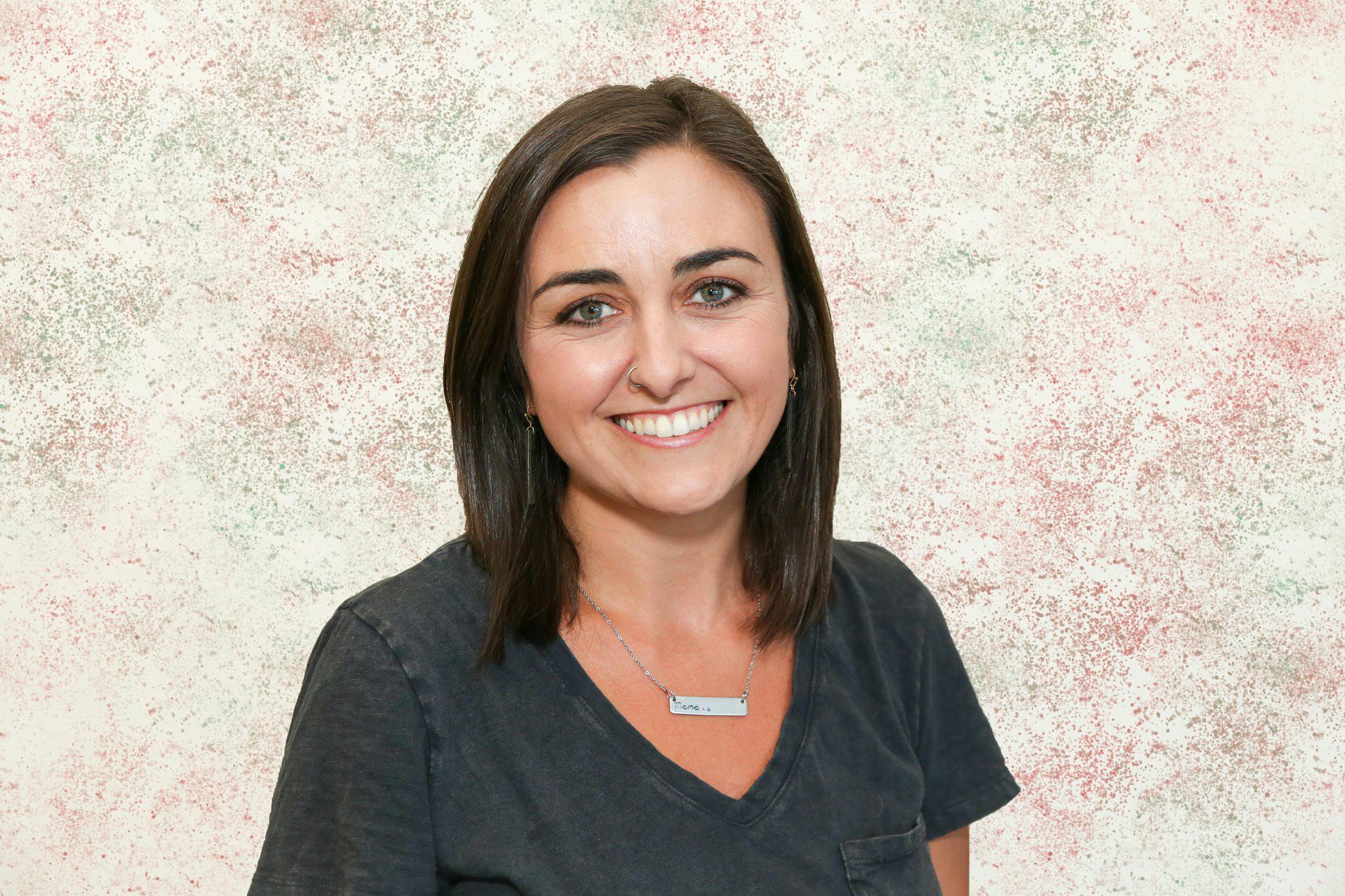 Person with brown hair wearing a dark grey shirt and a necklace