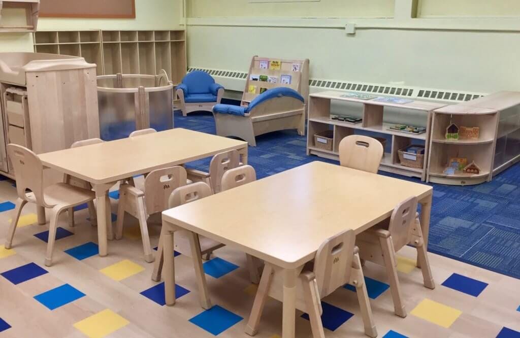 Classroom with small tables and chairs, shelves, and blue and yellow floor tiles