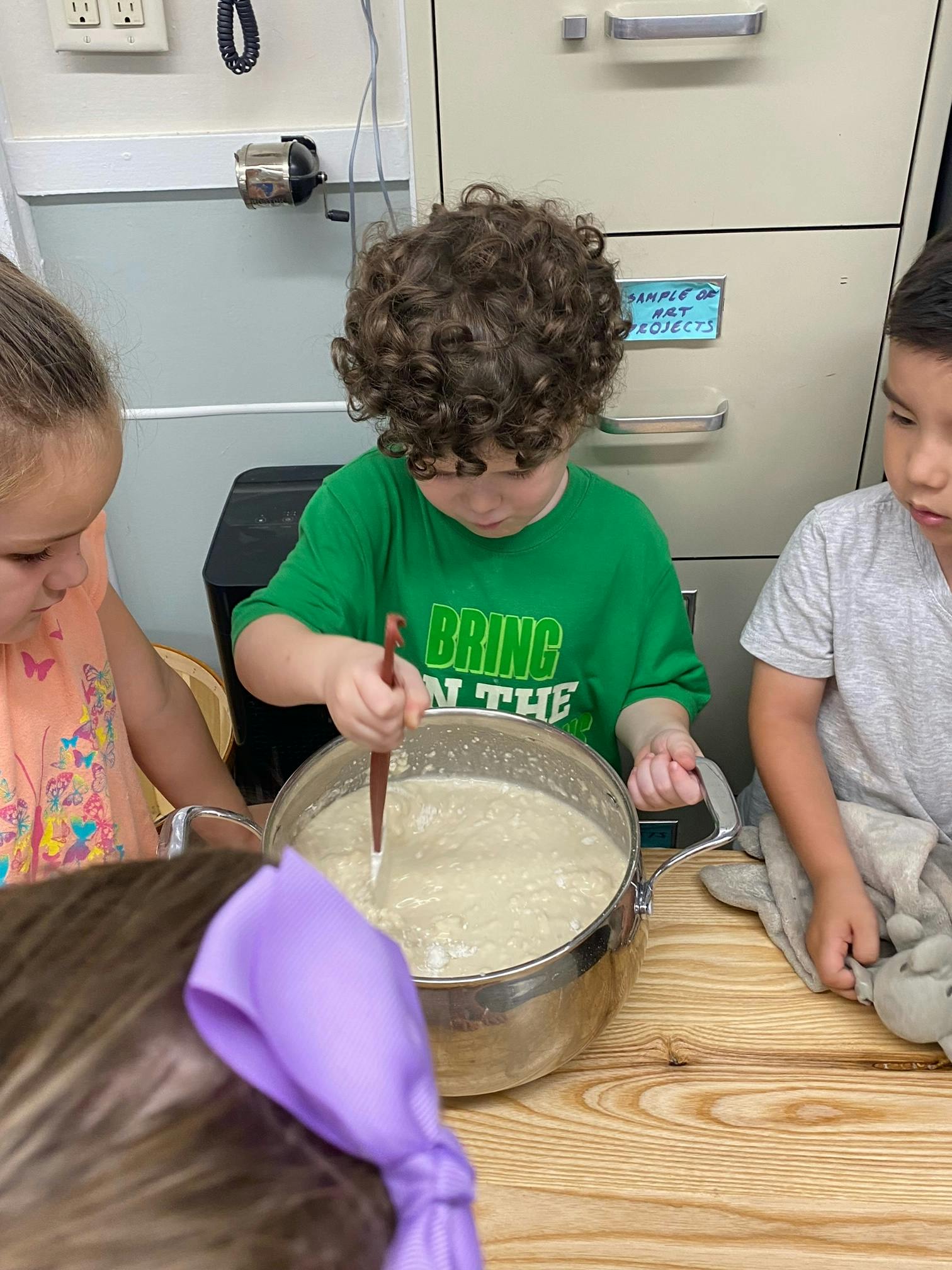 Child stirring a pot of liquid with other children nearby