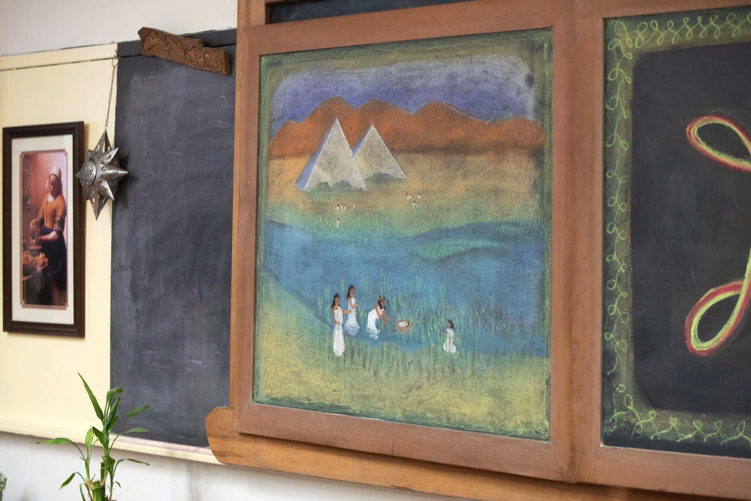 Chalkboard drawing of pyramids, mountains, people in water, and a baby in a basket