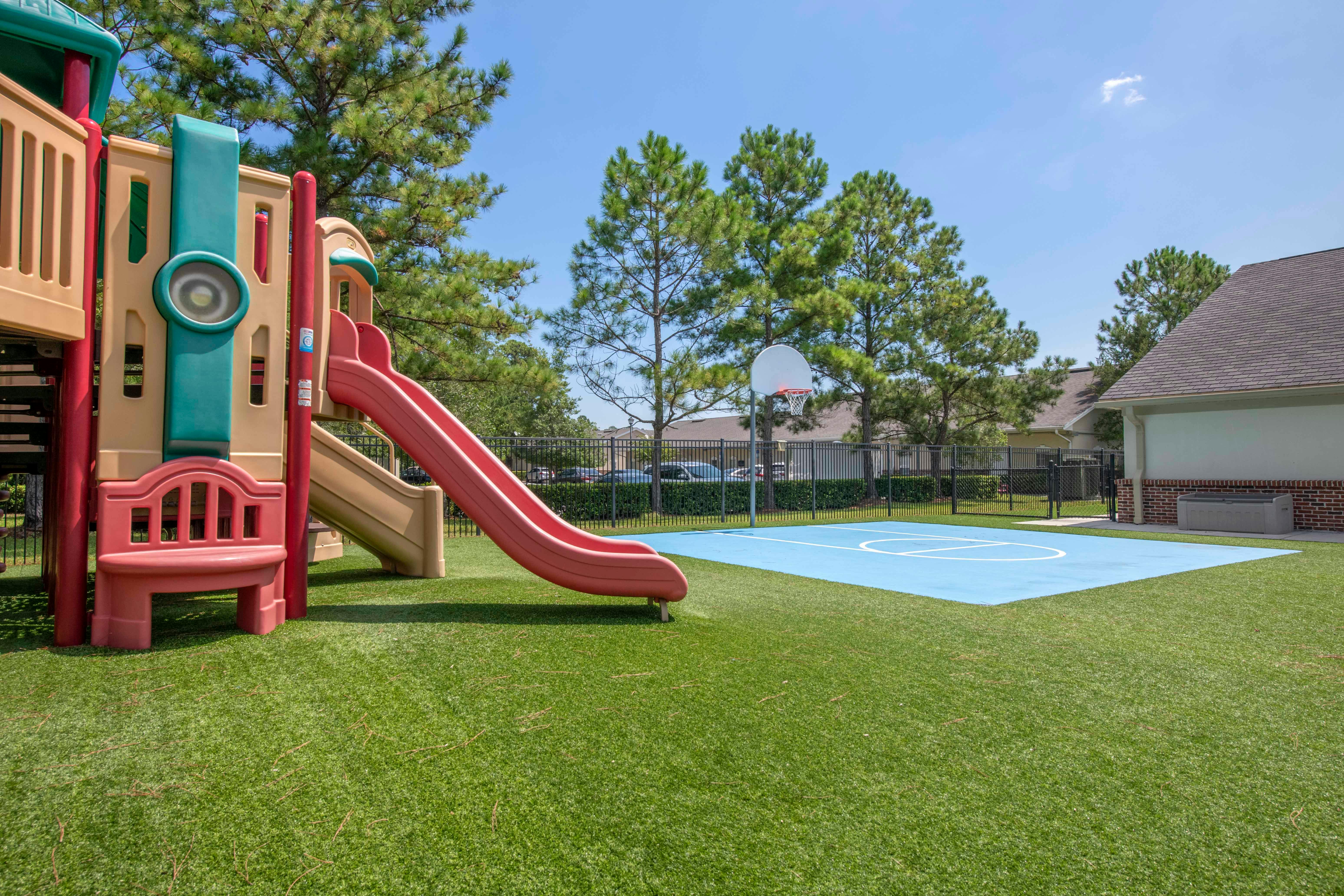 Playground set with red slide next to a blue basketball court with a hoop