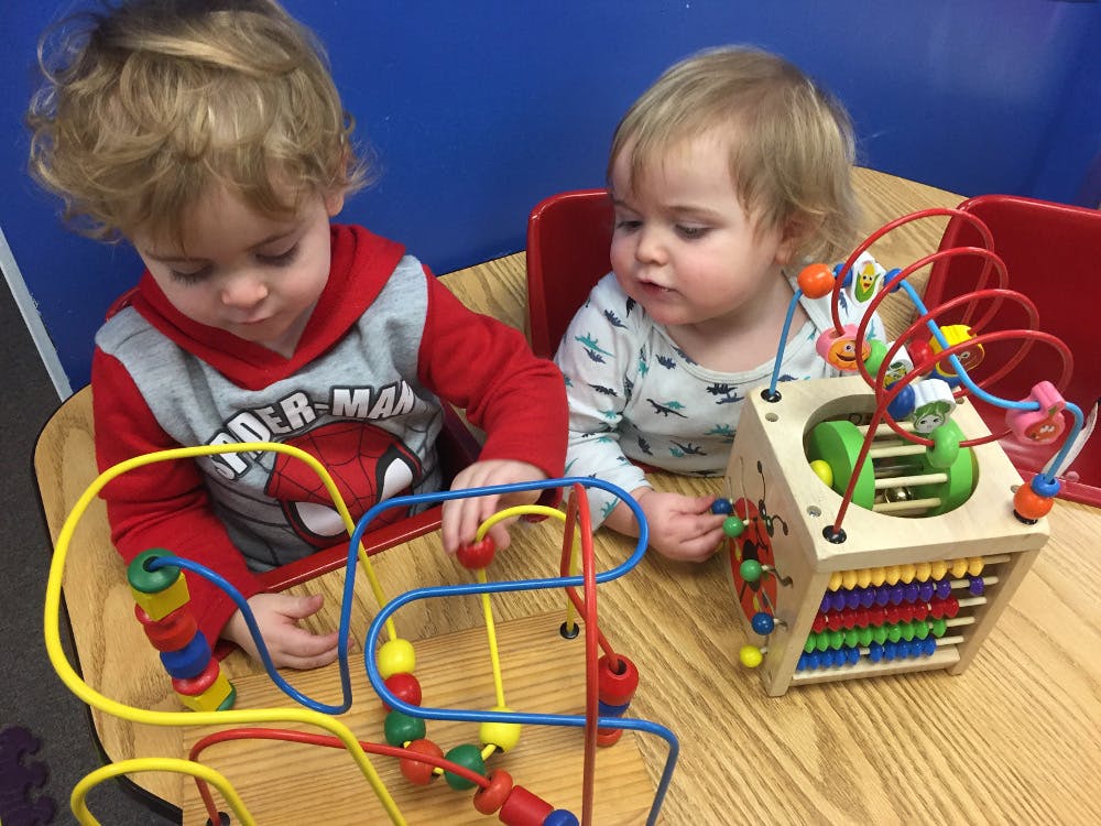 Two children playing with bead maze toys on a table