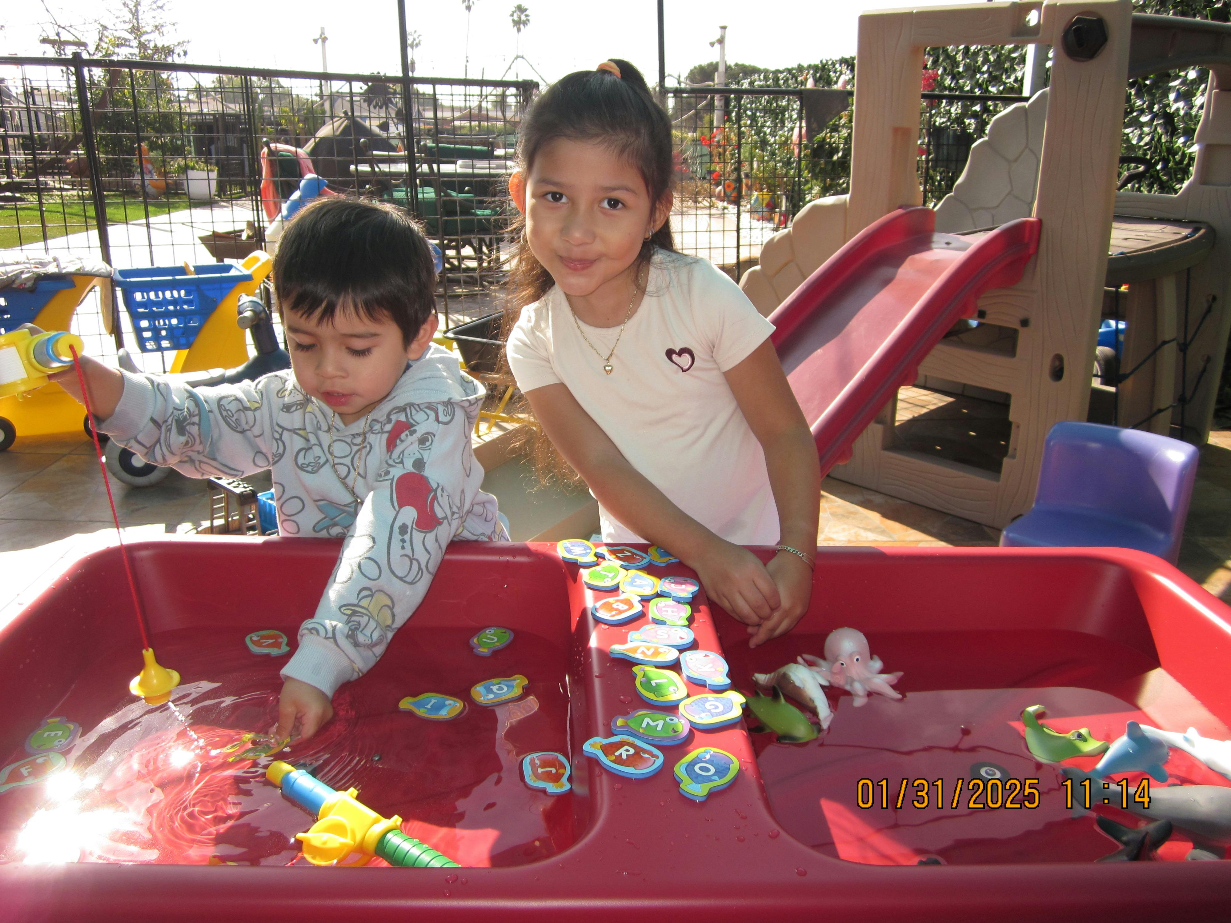Two children playing with toys in a water table