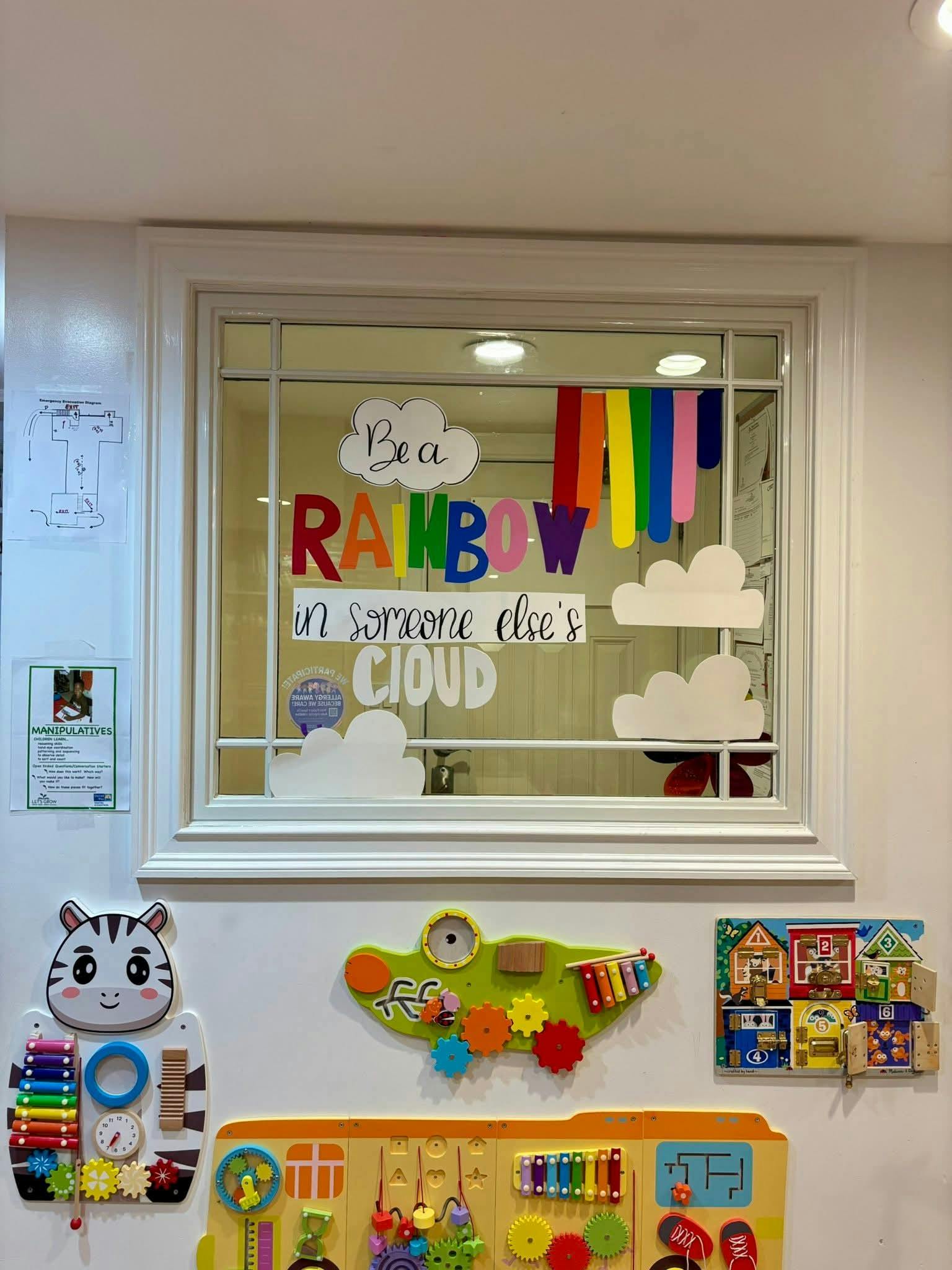 Window with "Be a rainbow in someone else's cloud" text and colorful decorations