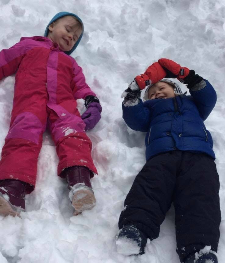 Two children in winter clothing lying in the snow