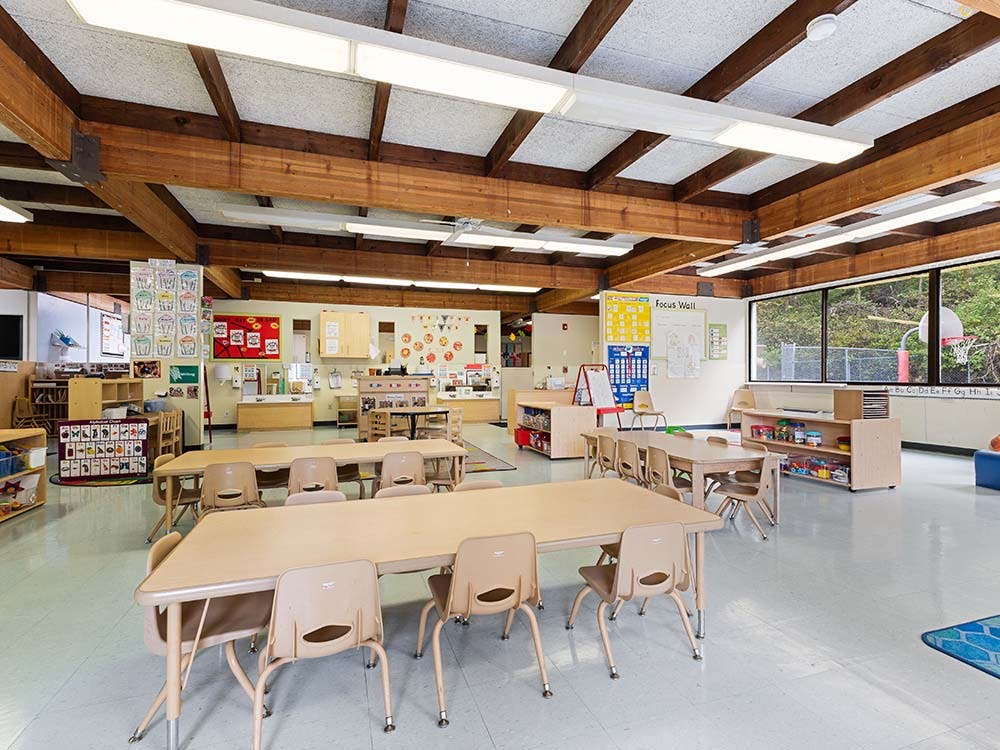 Empty classroom with small tables and chairs, and bright windows