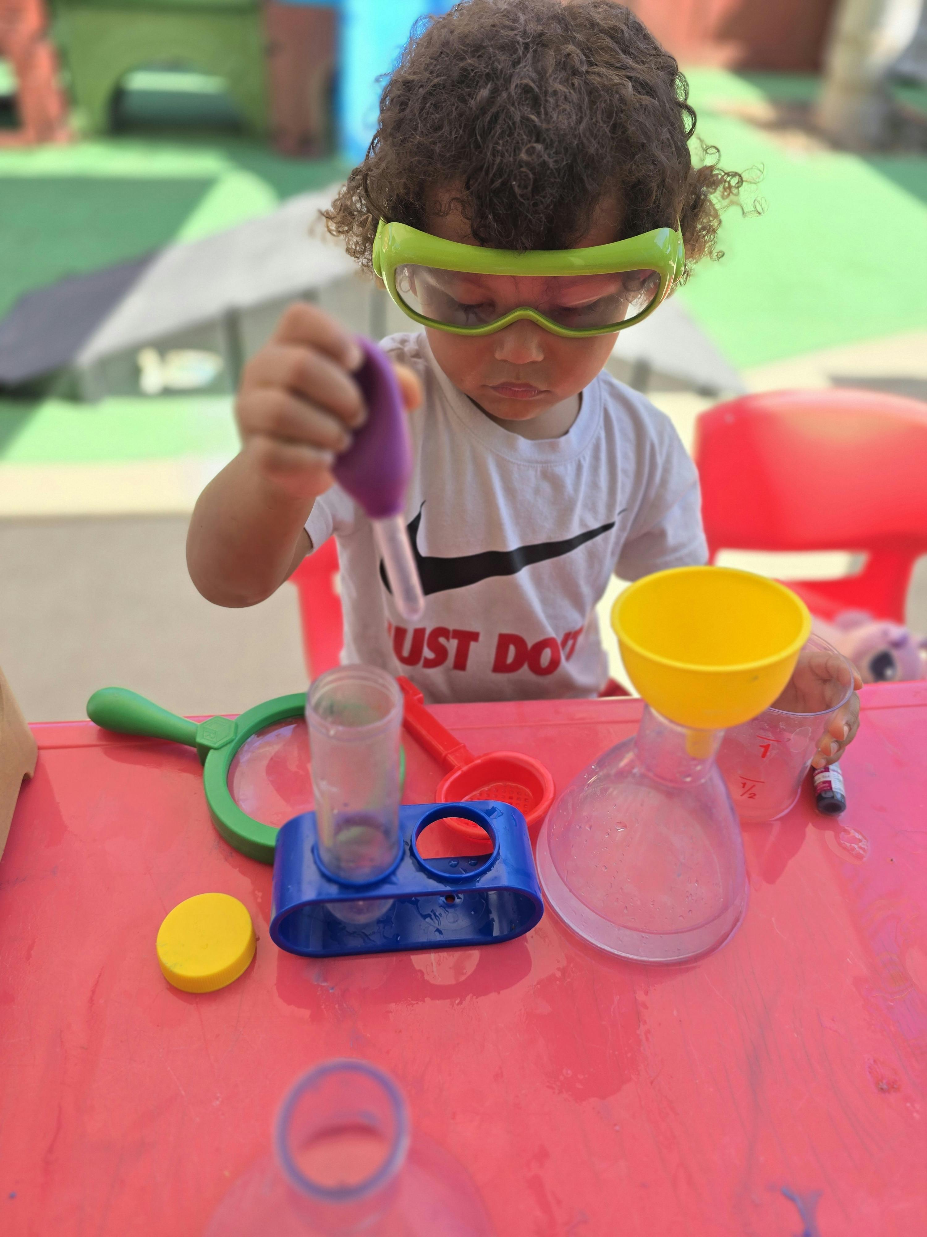 Child wearing protective goggles using a pipette for a science activity