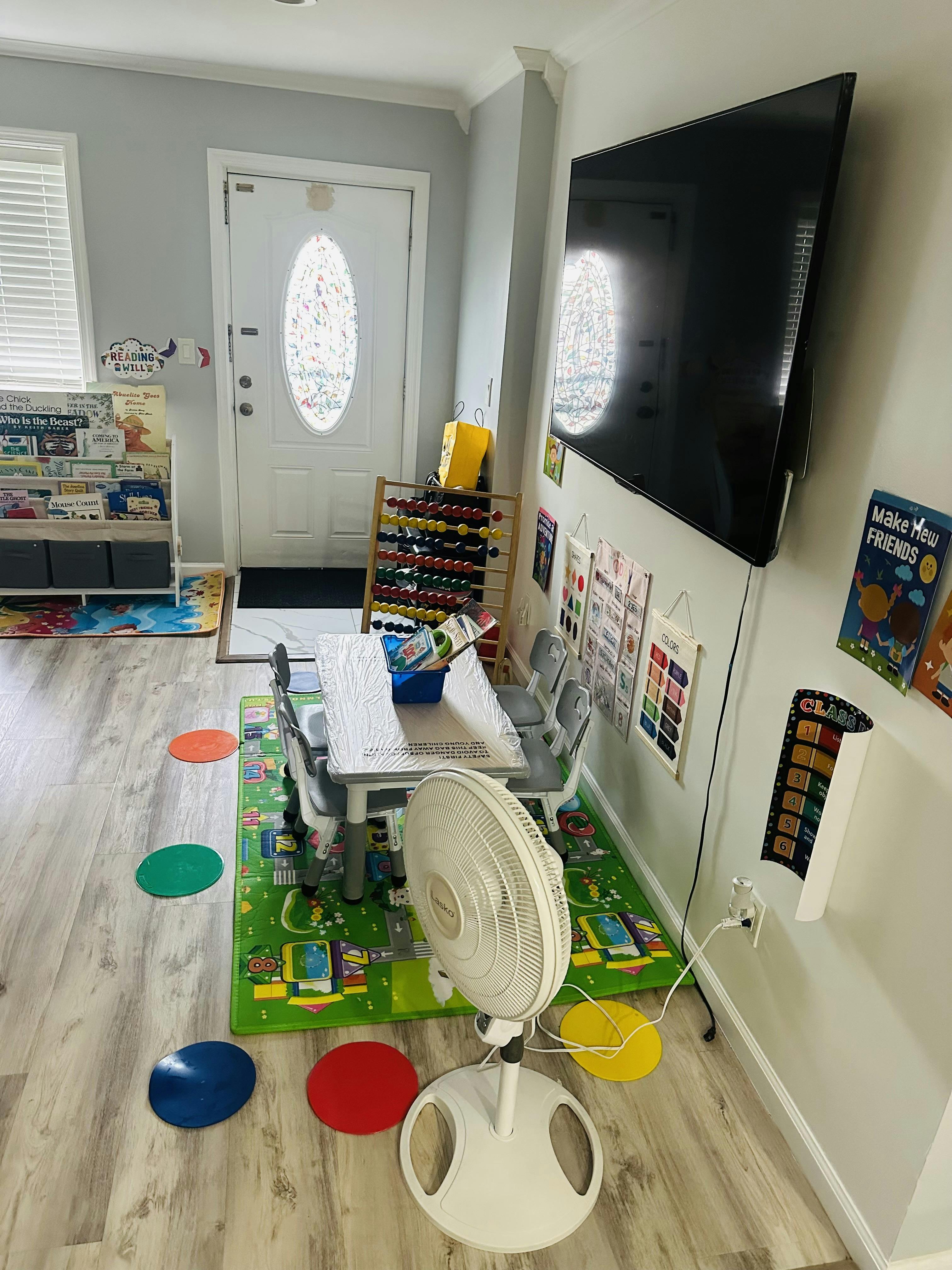 Classroom with small table and chairs, wall-mounted TV, and colorful floor mats
