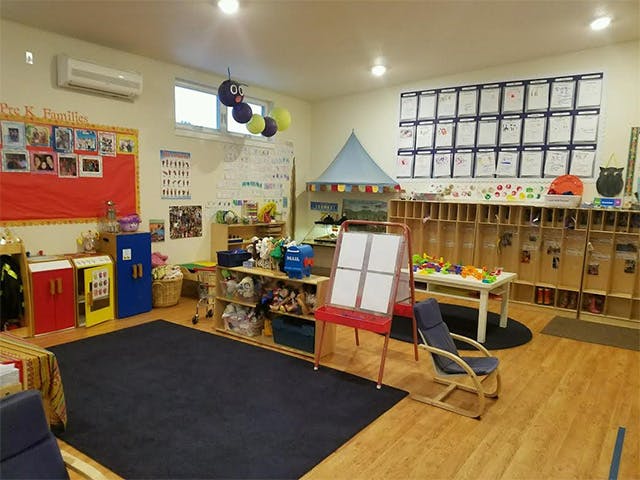 Classroom with a dark rug, small tables, shelves, and an easel