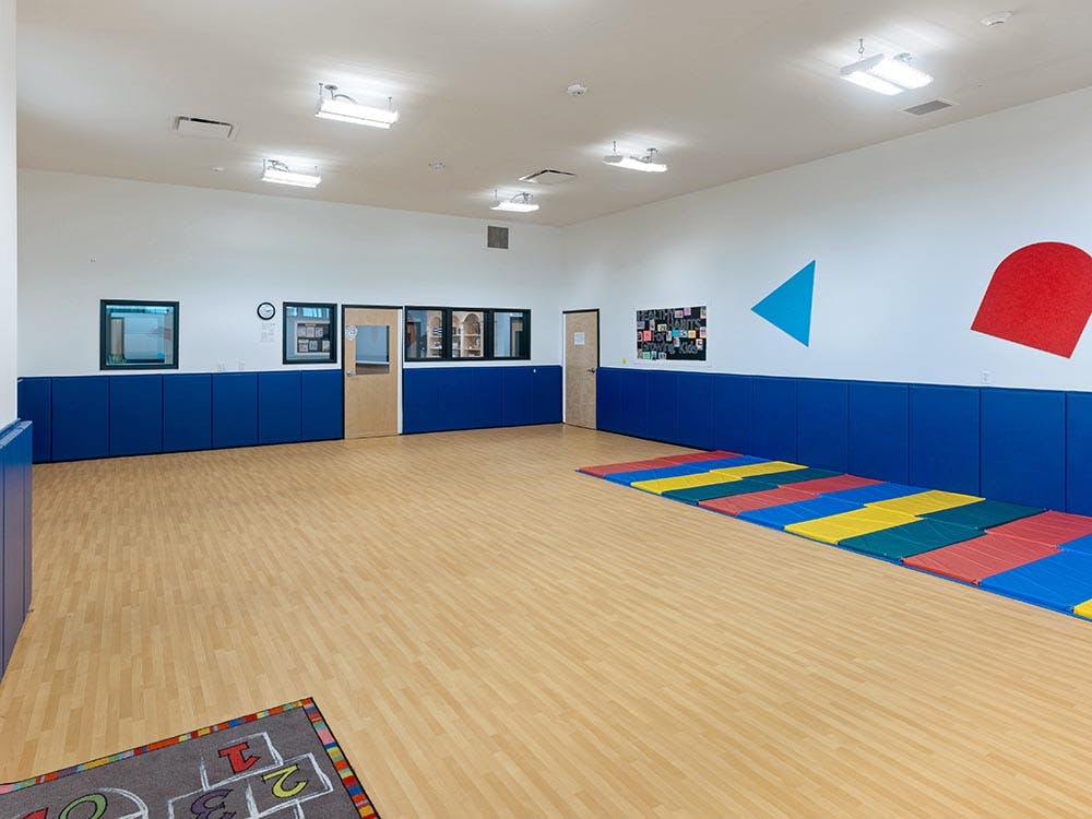 Empty classroom with blue padded walls, colorful floor mats, and a hopscotch rug