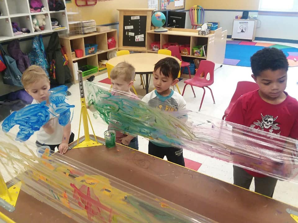 Children painting on clear plastic sheets in a classroom