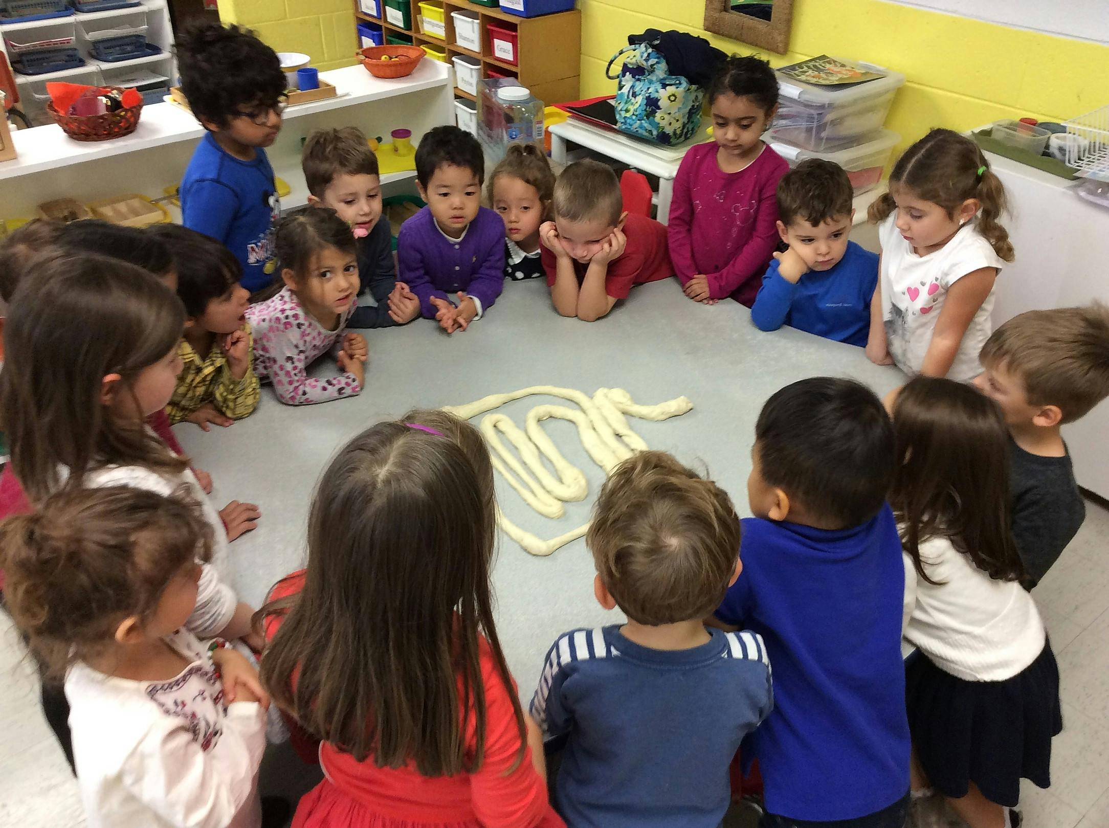 Children gathered around a table looking at a white, squiggly object