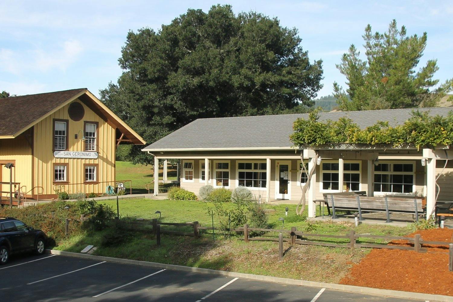 Two buildings with green lawns and trees, with a parking lot in the foreground