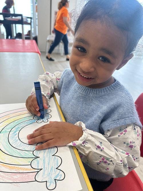 Child coloring a rainbow drawing with a blue crayon