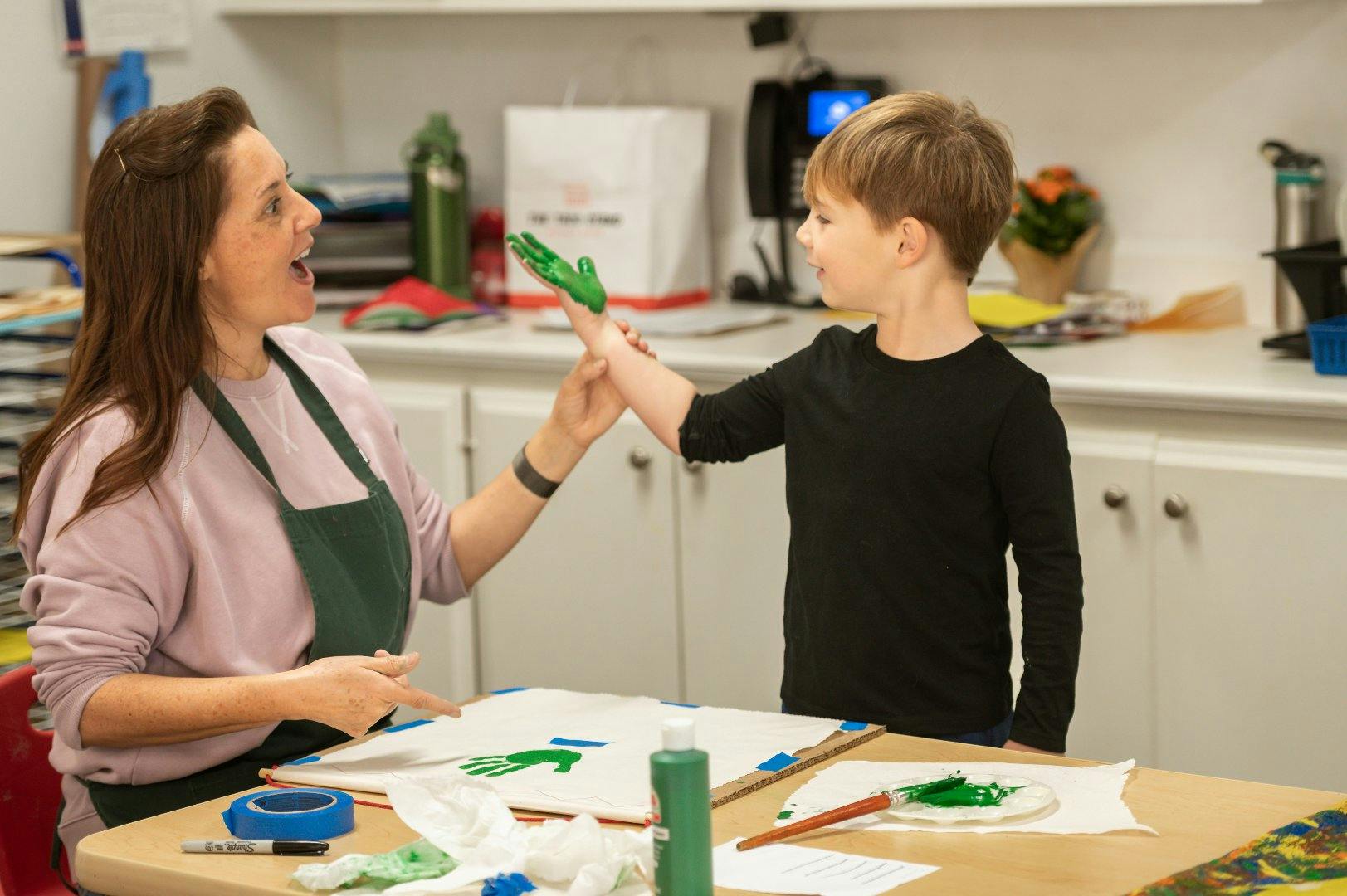 Adult and child with green paint on their hands making a handprint on paper