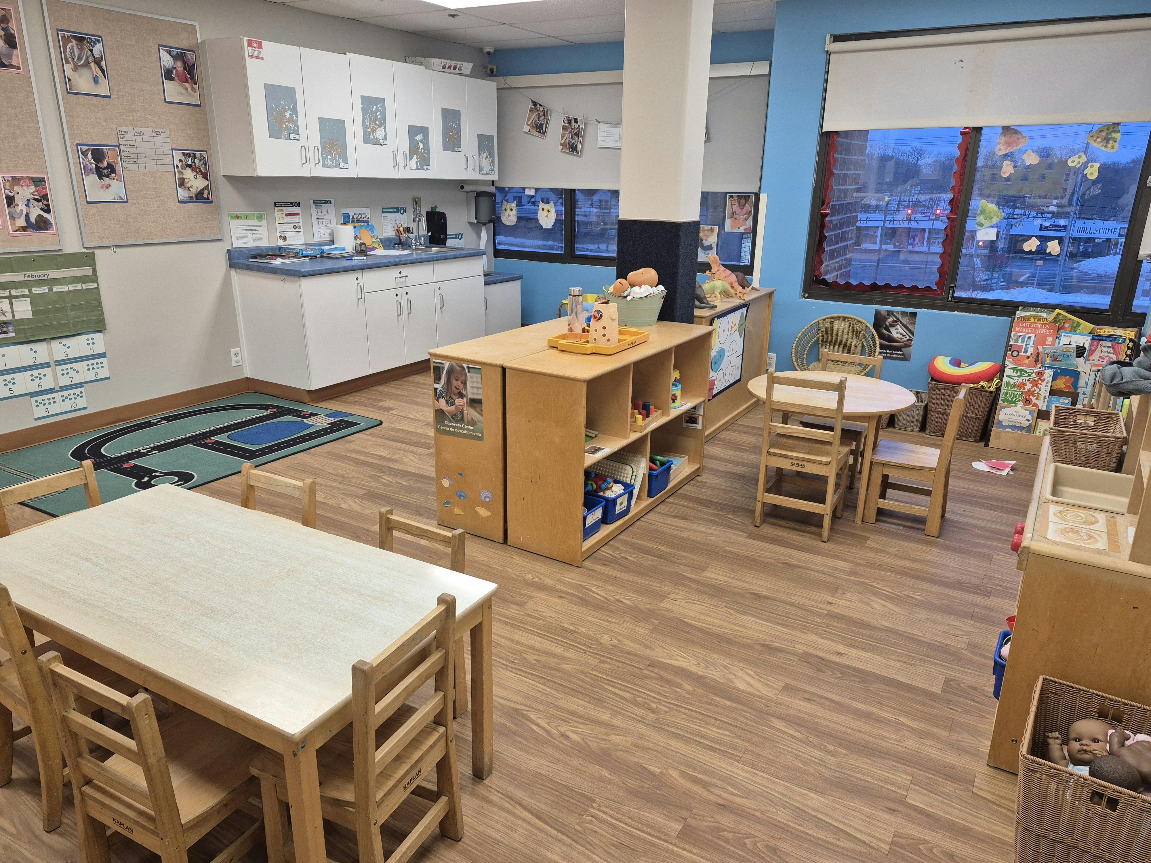 Classroom with child-sized tables and chairs, play kitchen, and toy shelf