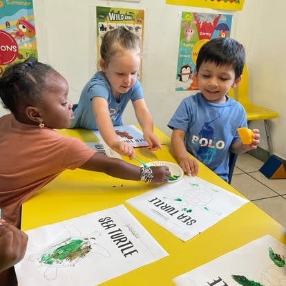 Three children painting sea turtle pictures at a yellow table