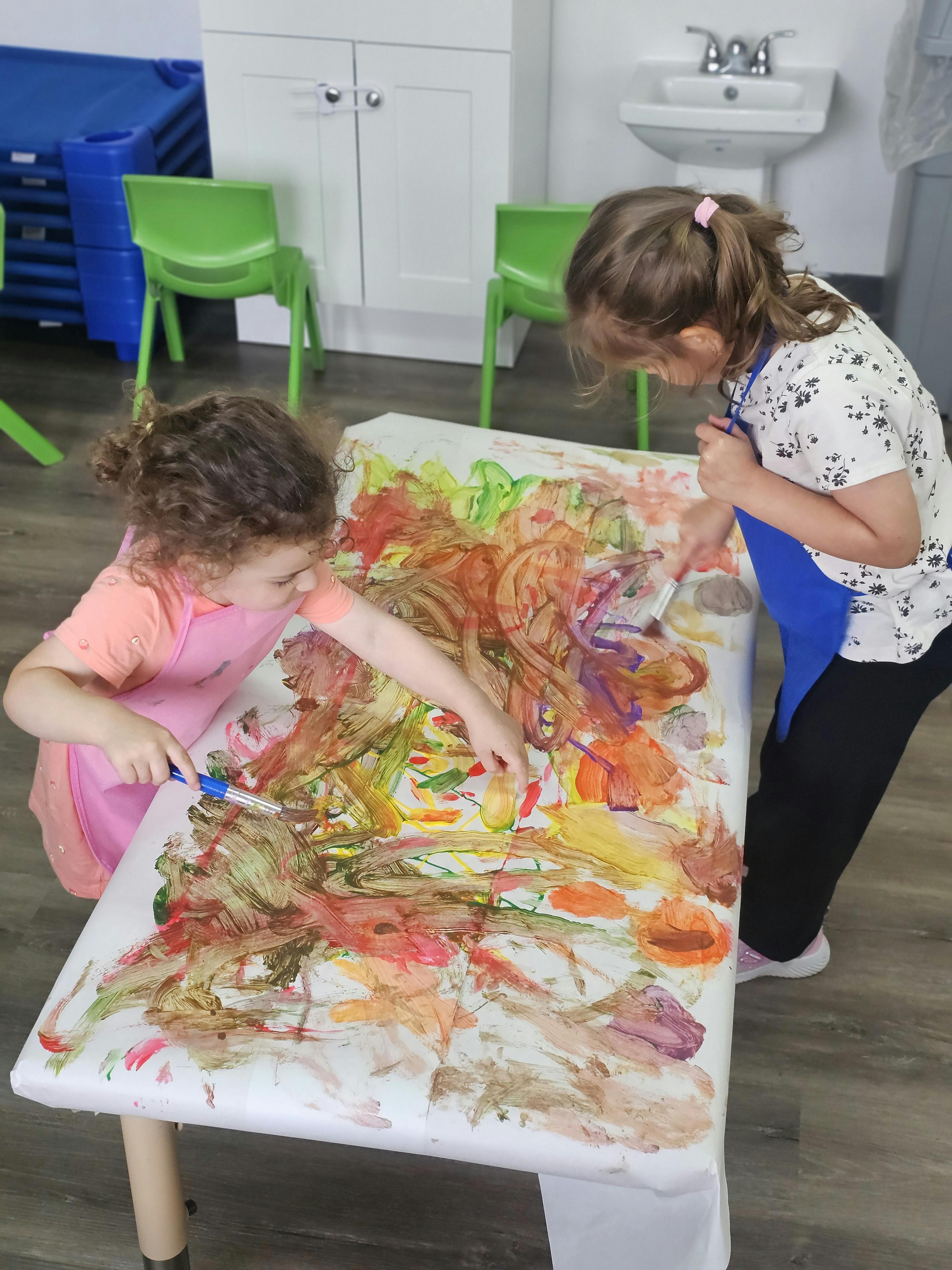 Two children painting on a large sheet of paper at a table