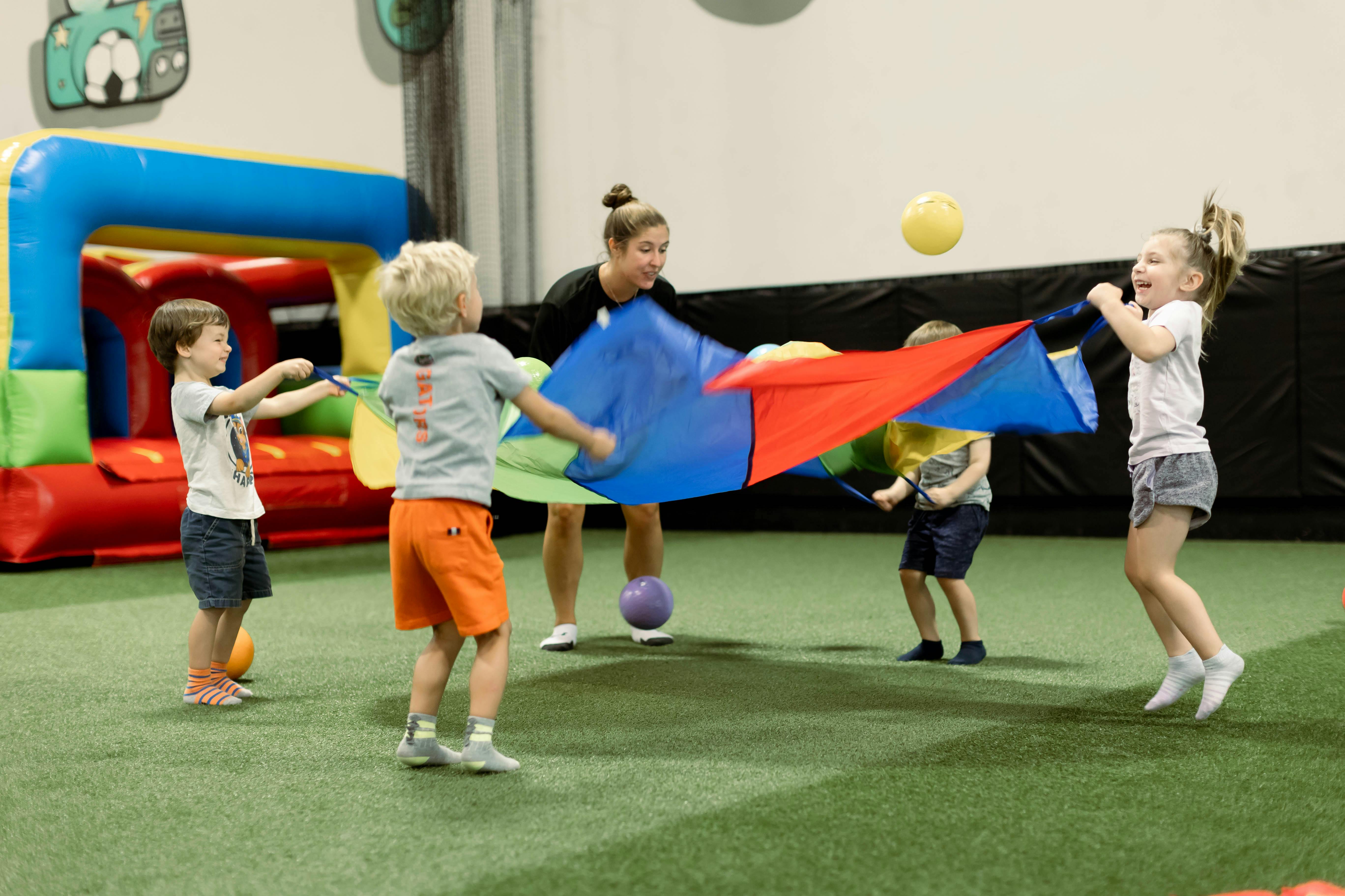 Adult and children playing with a colorful parachute and balls indoors