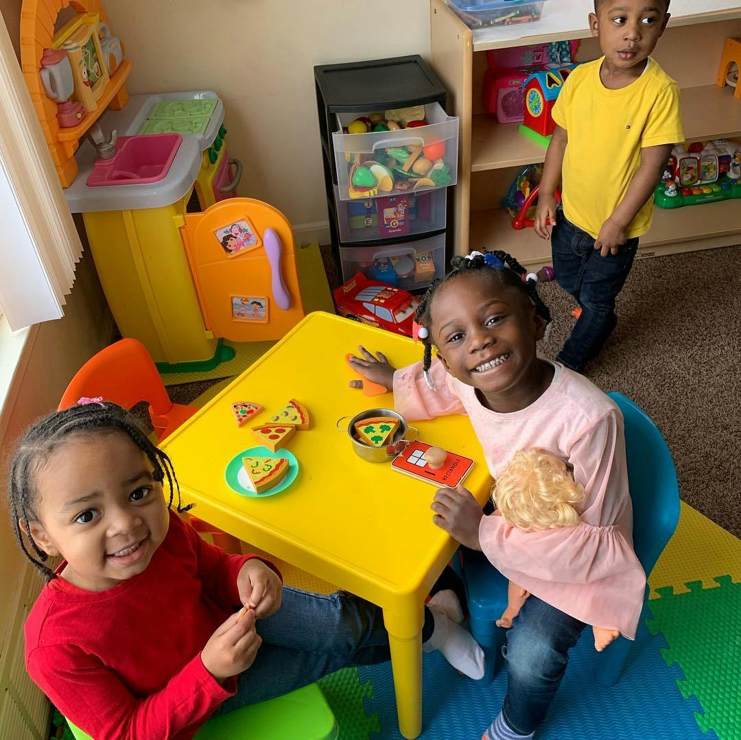 Three children playing with toy food at a yellow table