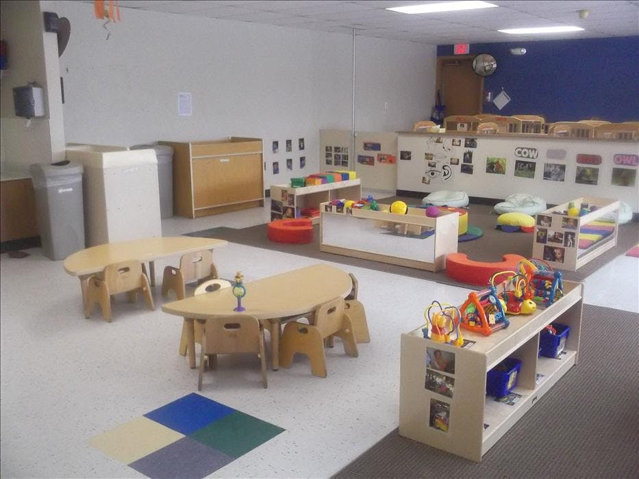 Empty classroom with small tables and chairs, shelves, and toys on the floor