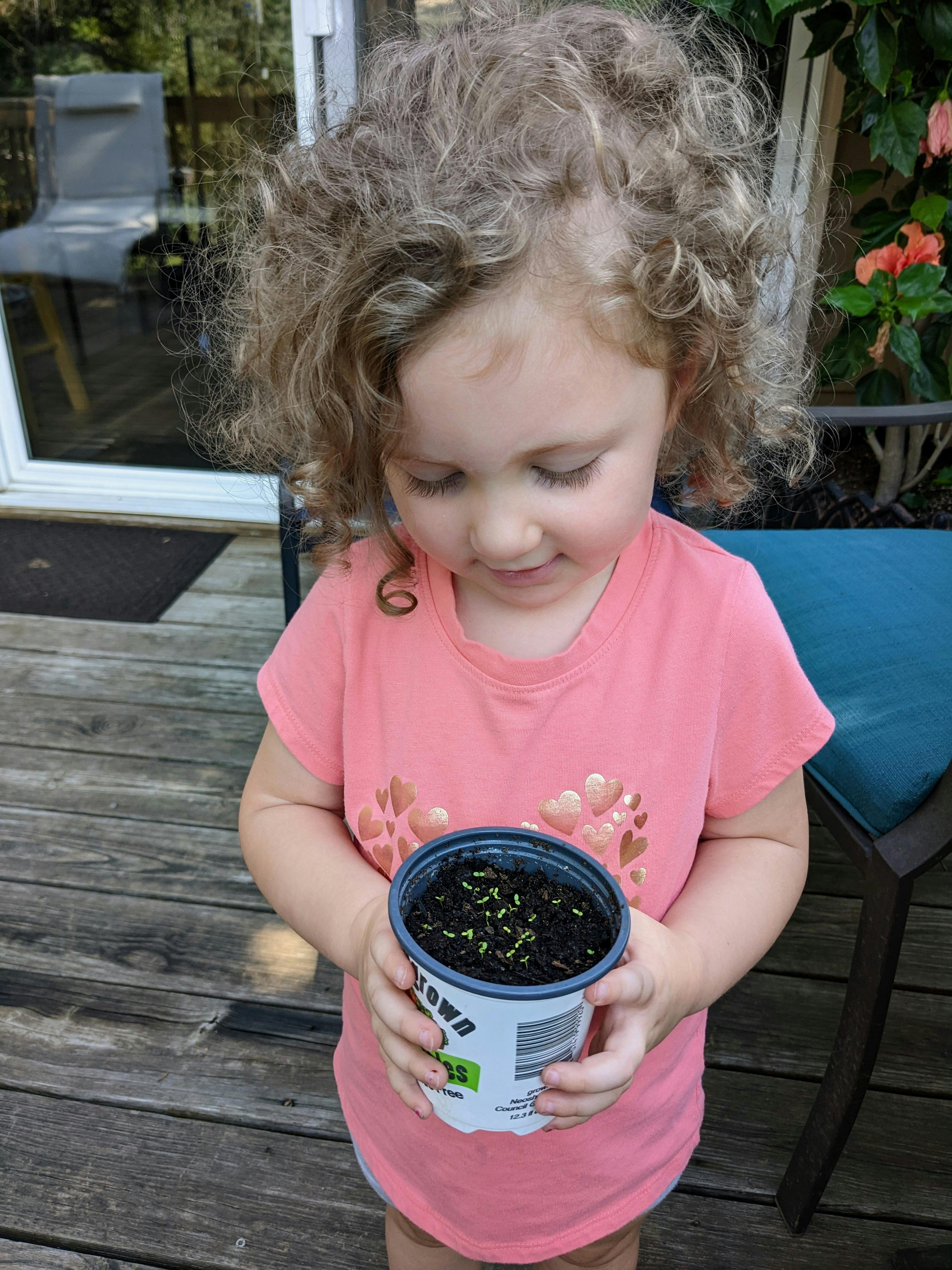 Child holding a small pot with soil and tiny green sprouts