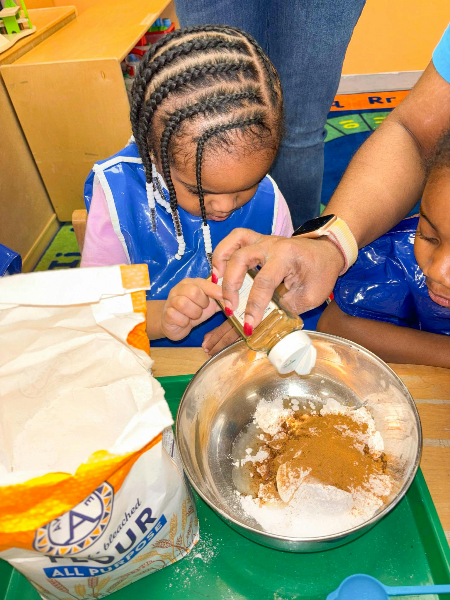 Child watching person sprinkle spice into a bowl of flour