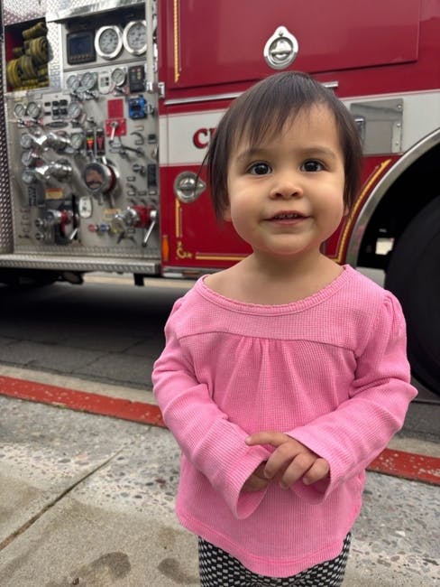 Child in pink shirt standing in front of a fire truck