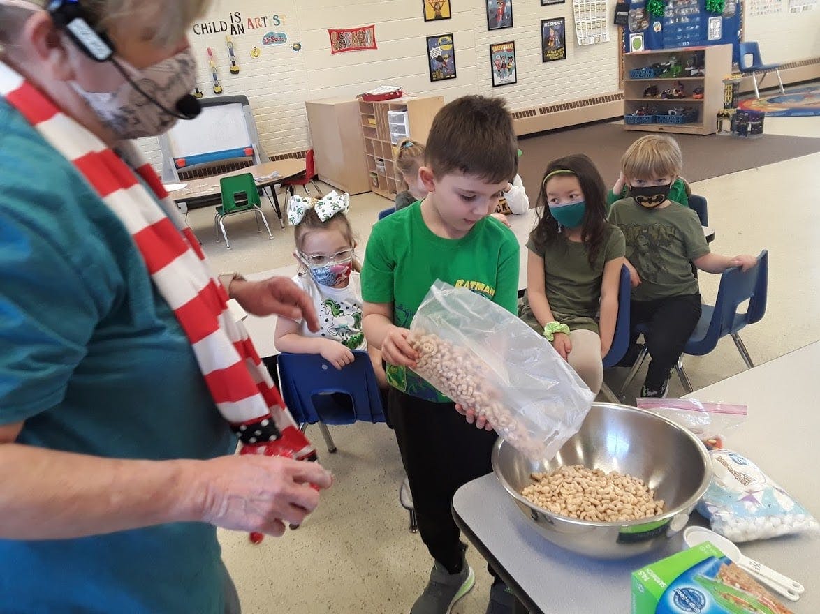 Adult and child pouring cereal into a bowl with other children watching