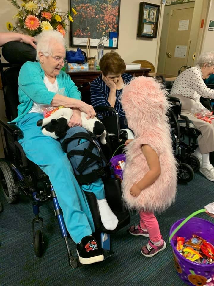 Person in wheelchair holding a stuffed animal, child in pink costume with candy bucket