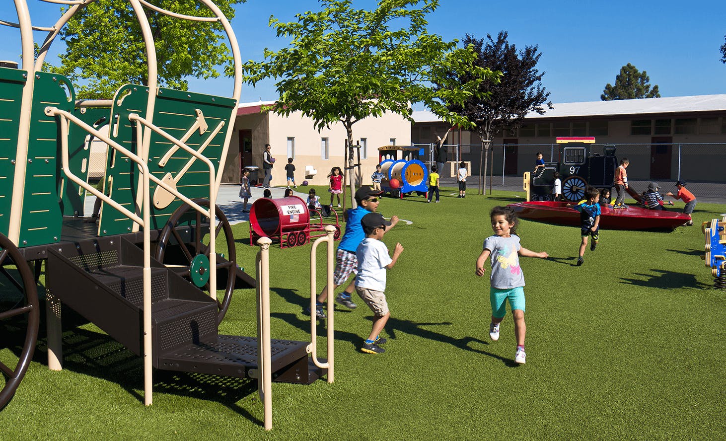 Children playing on a playground with structures and green turf