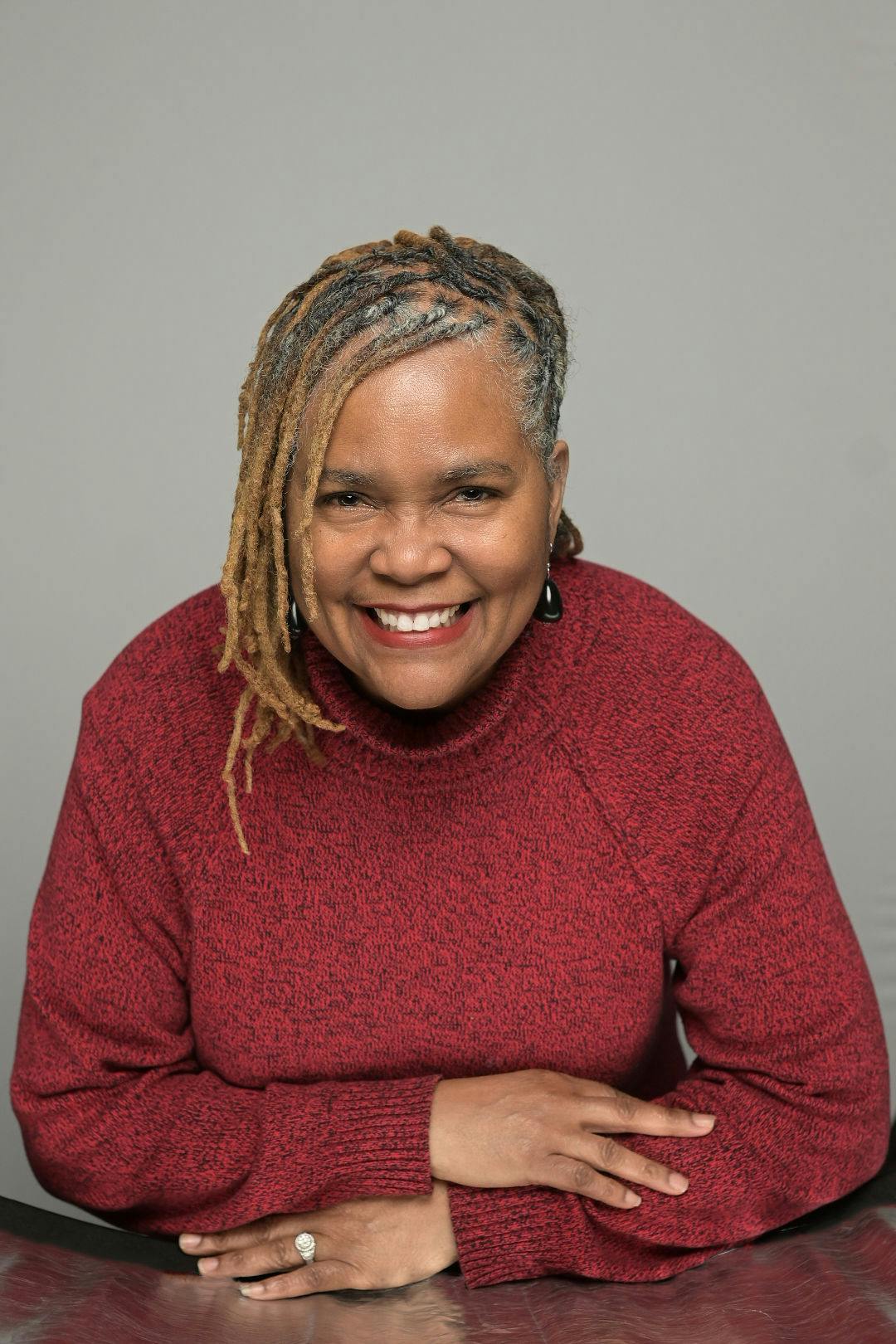 Person with dreadlocks in a red sweater smiling